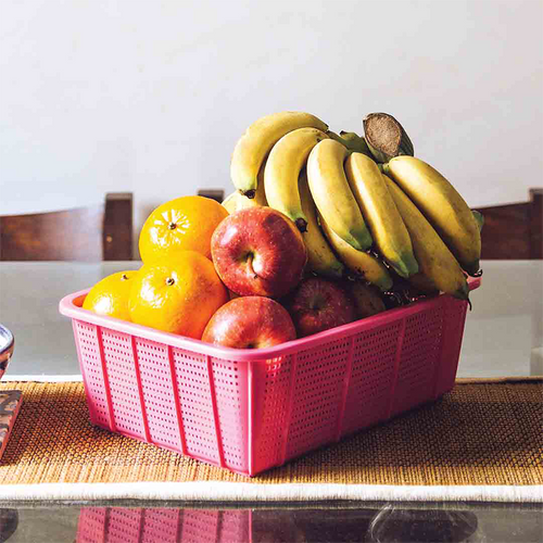 Fruit basket with bananas, apples, and oranges in a pink plastic basket on a table.